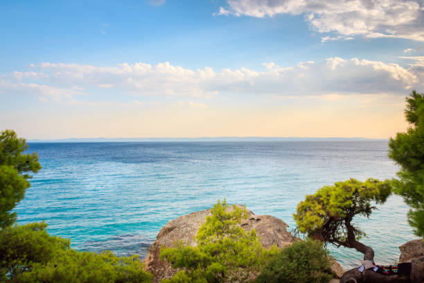 Sun rays, clouds and turquoise sea water of Koviou beach and beautiful rocks and curvy, horizontal tree